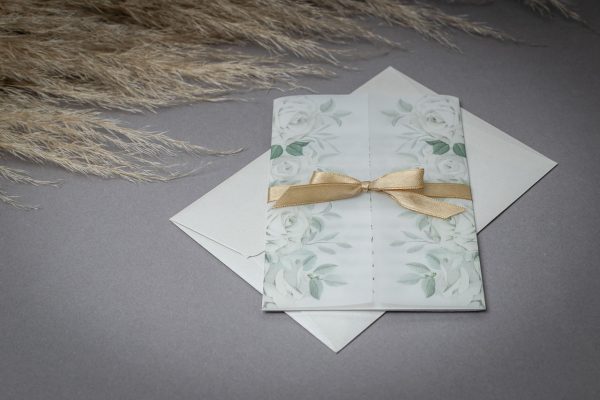 Elegáns esküvői meghívó gyöngyház papírra nyomtatva, virágmintás pauszpapírral és szatén szalaggal díszítve.